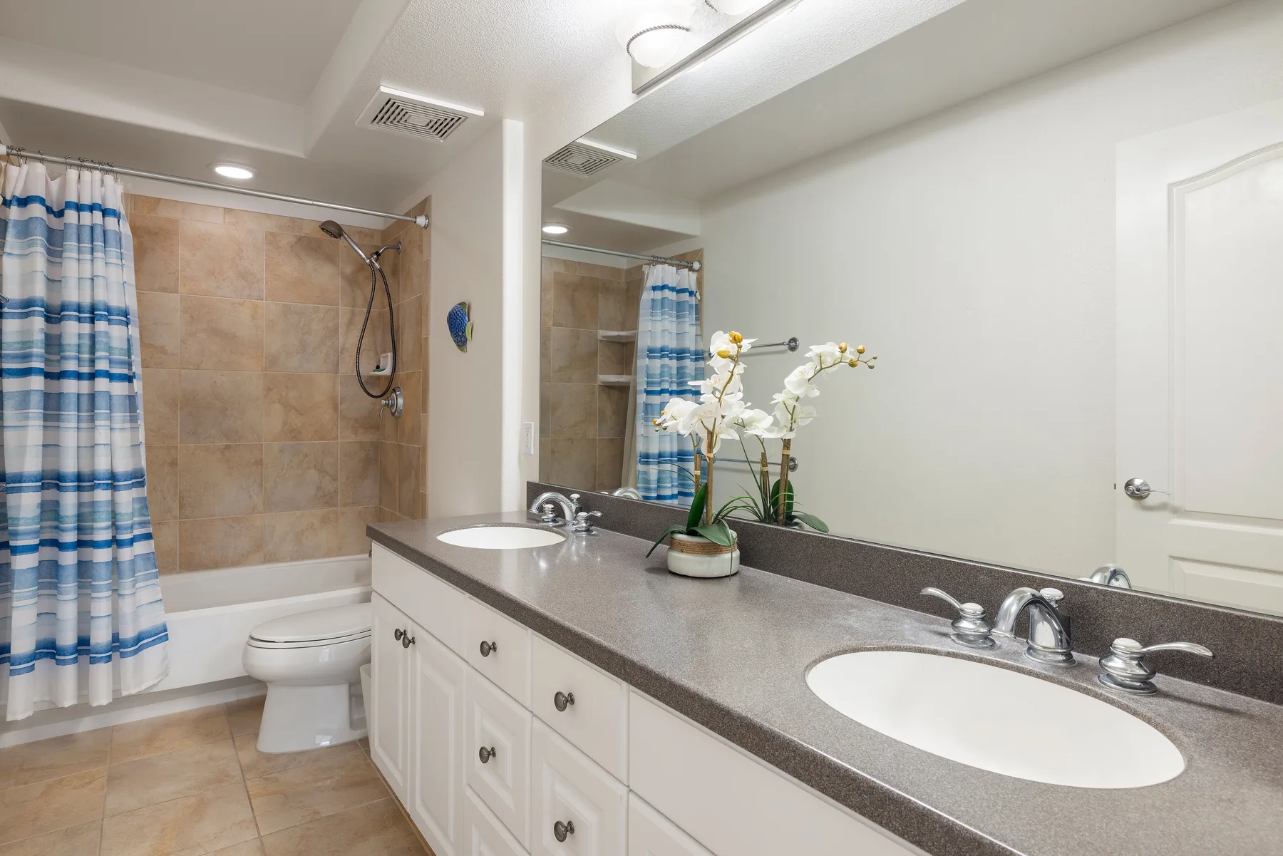 A bathroom with a long vanity, mirror, and tub-shower behind a striped curtain.