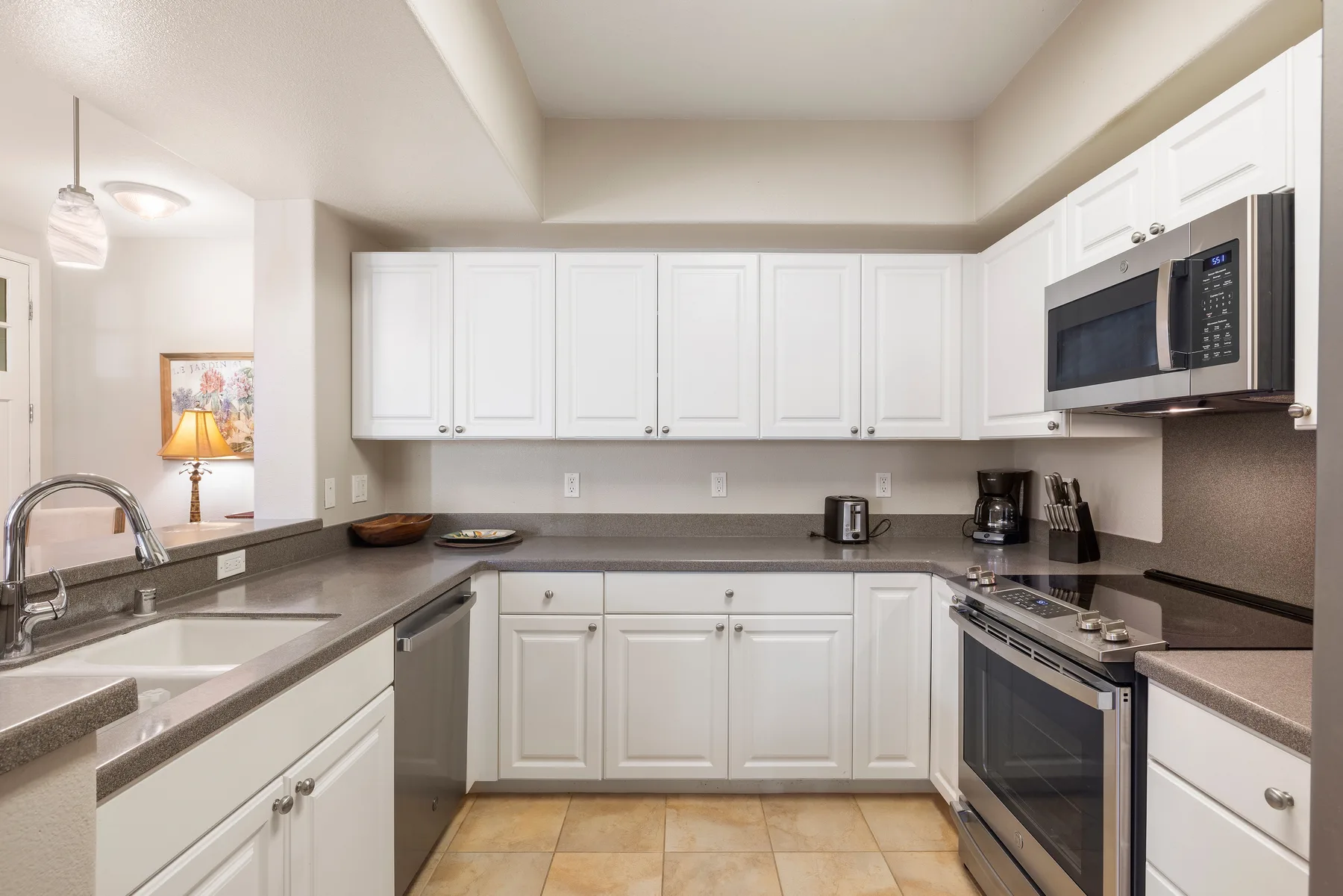 A bright kitchen with white cabinets, dark countertops, and stainless-steel appliances.