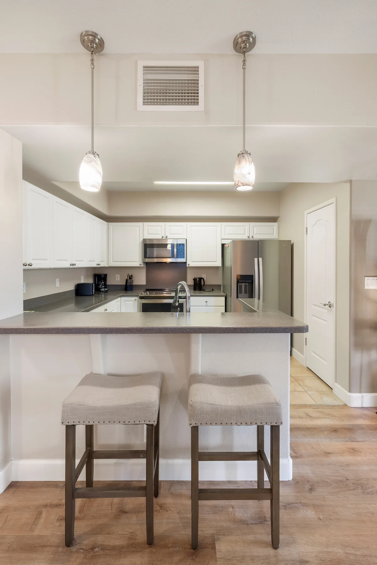 A bright kitchen with white cabinets, stainless steel appliances, and a counter with seating.