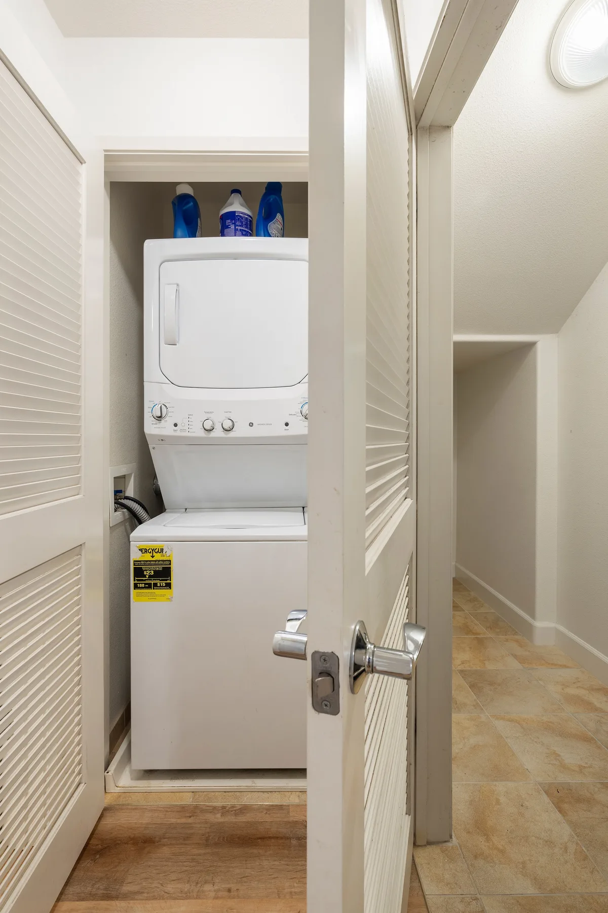 A laundry closet with a stacked washer and dryer behind a louvered door.