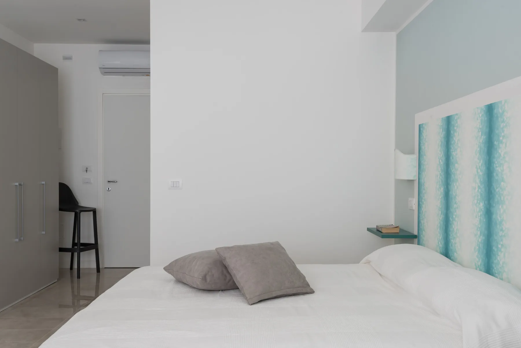 Un dormitorio luminoso con una cama y un cabecero estampado en tonos turquesa.