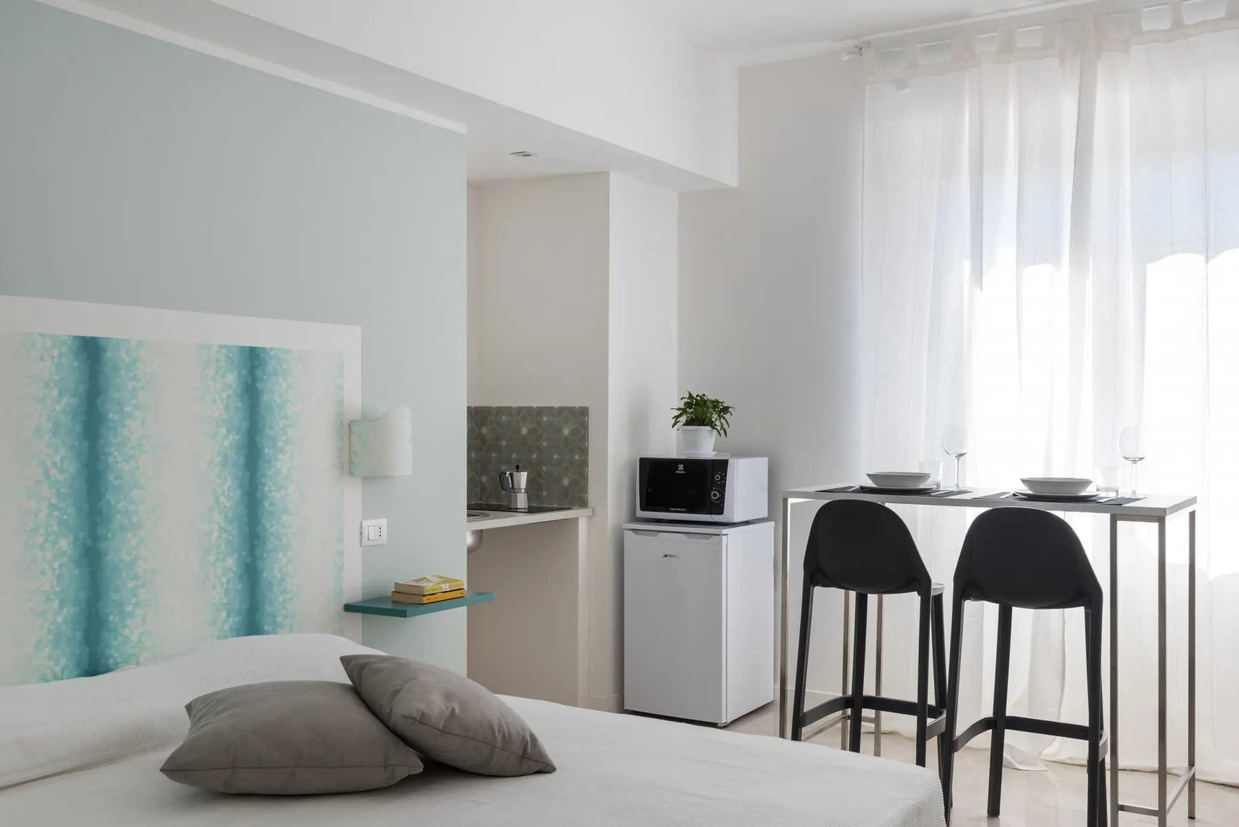 Un dormitorio luminoso con una cama, una mesa pequeña y cortinas translúcidas.