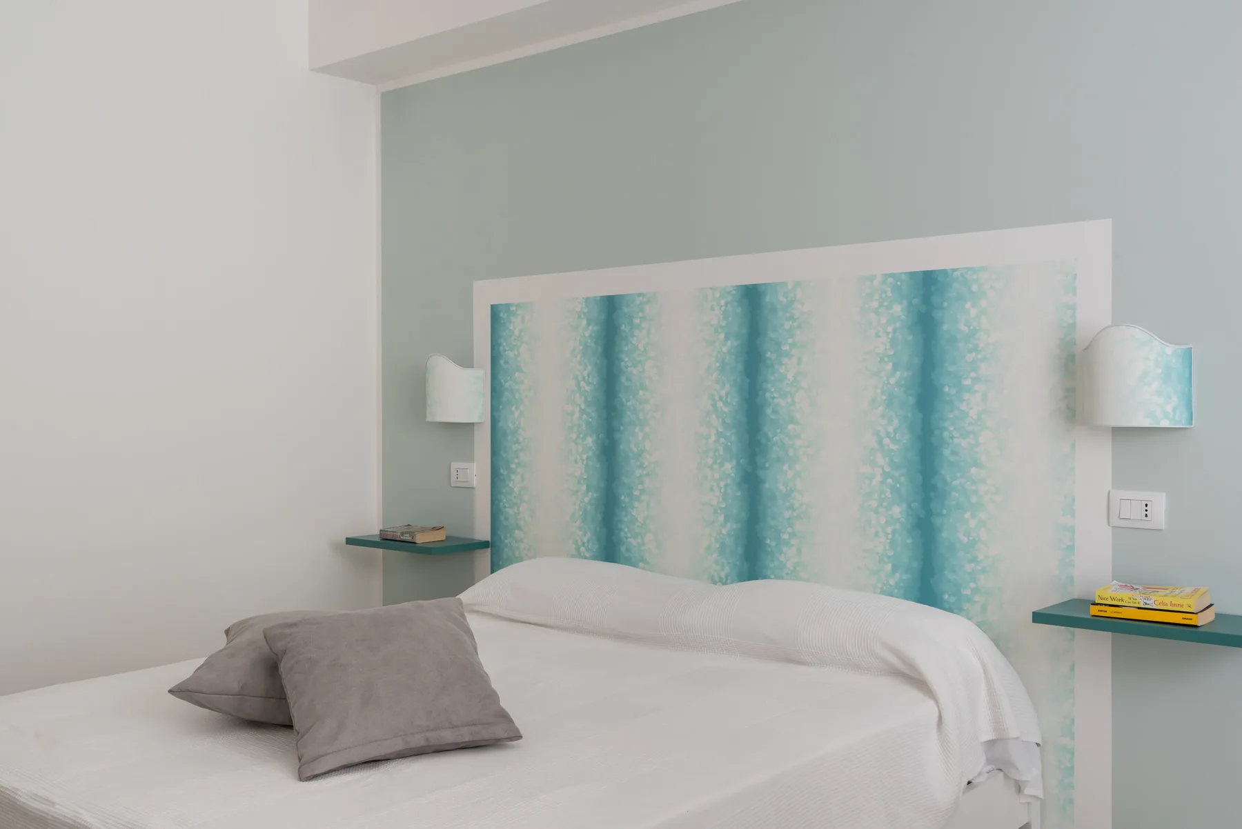 Un dormitorio con una cama, almohadas grises y un cabecero turquesa estampado.