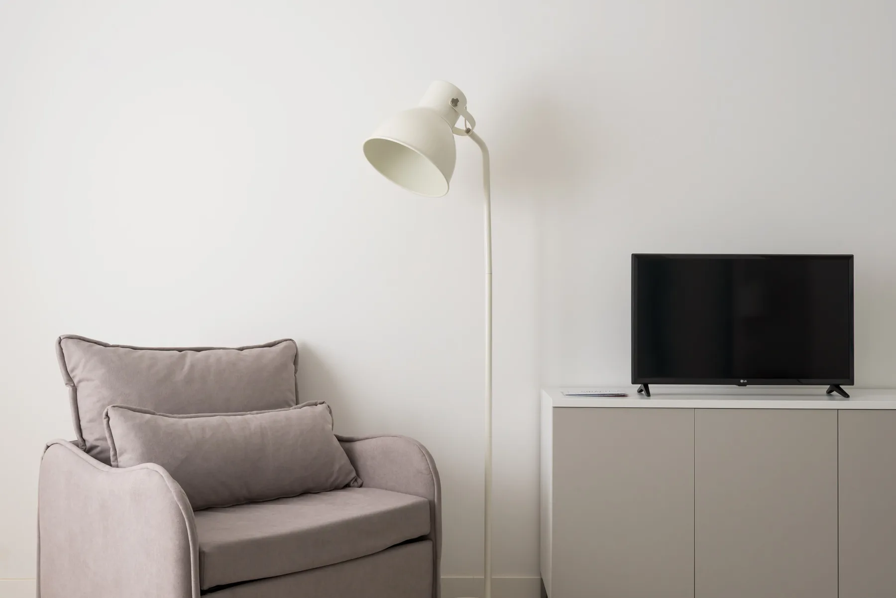 Una zona de estar con un sillón tapizado, una lámpara de pie y un televisor sobre un mueble.