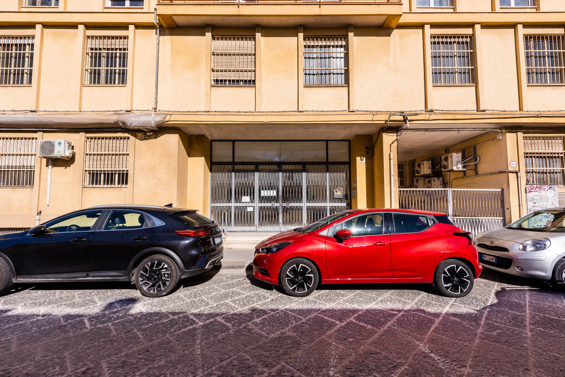Varios coches están estacionados en la calle frente a un edificio beige.