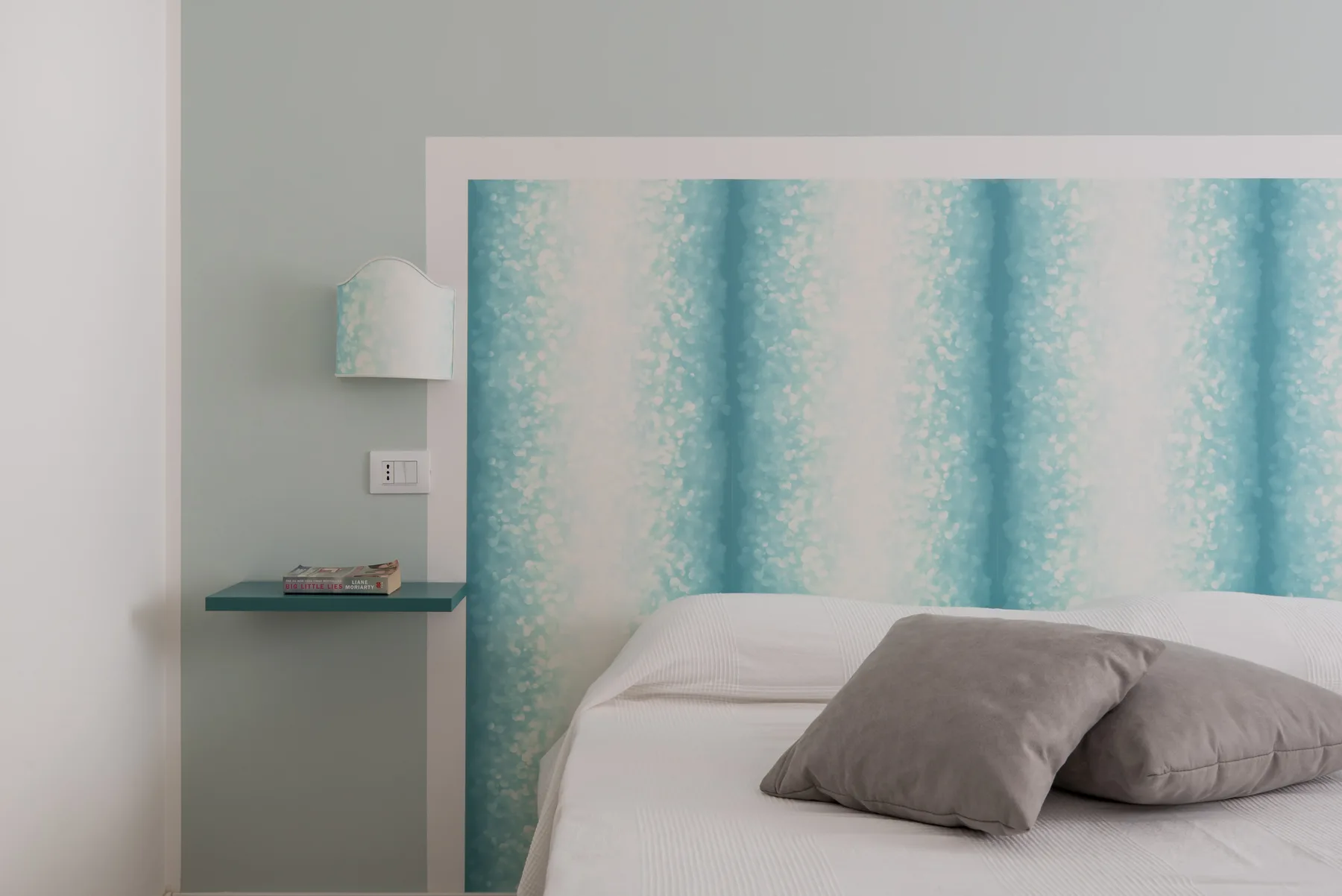 Un dormitorio con una cama y un panel de pared turquesa estampado.