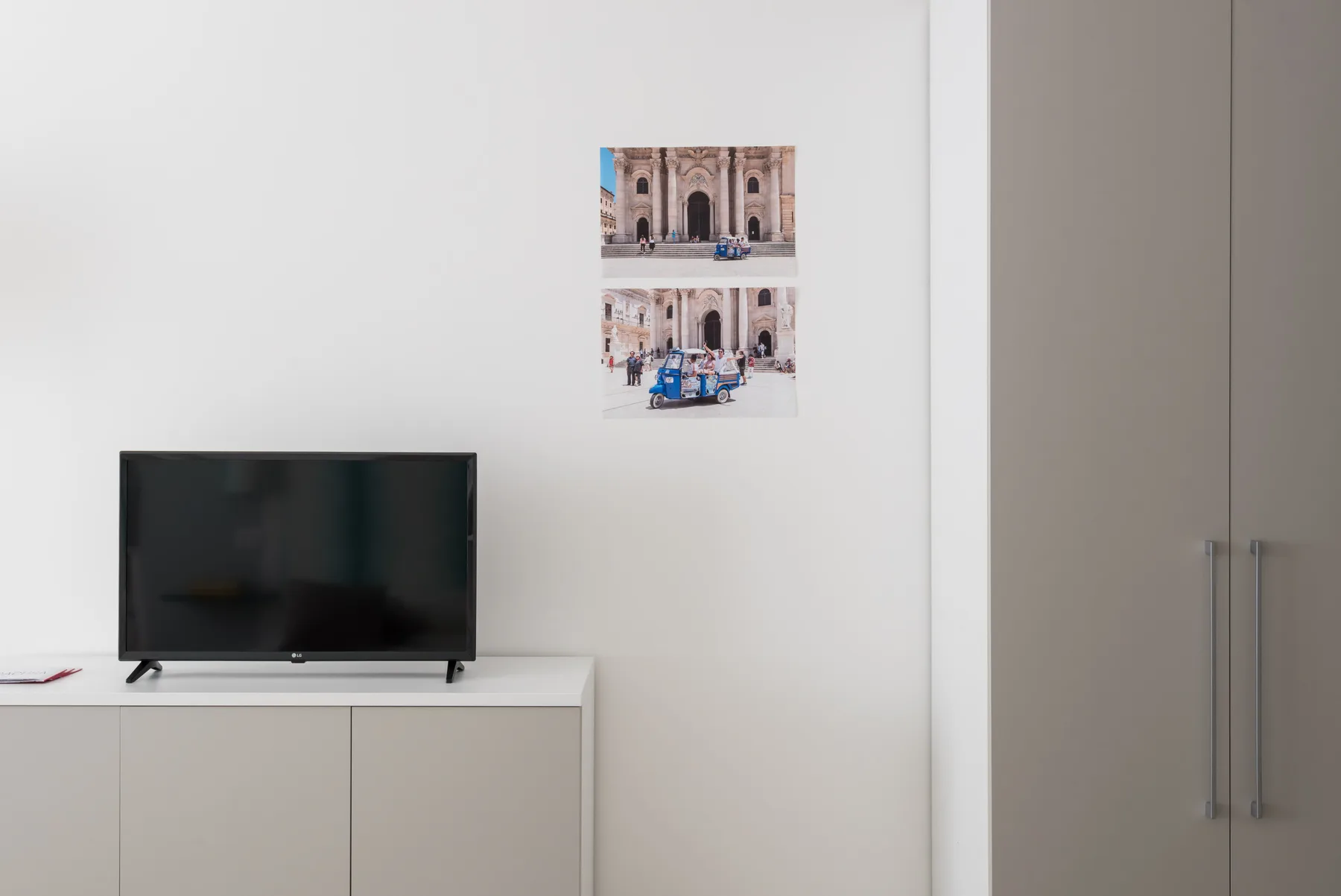 Una habitación luminosa con un televisor sobre un mueble bajo y dos imágenes en la pared.
