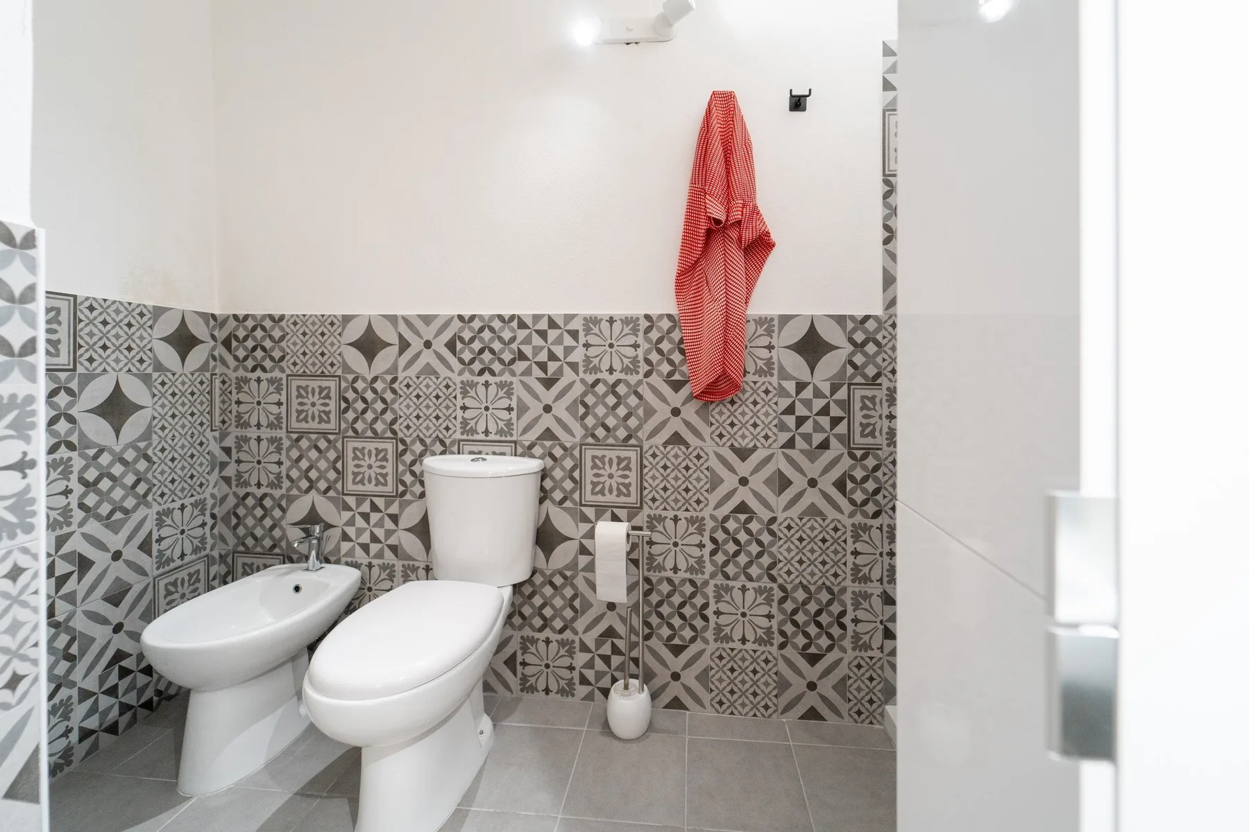 A tiled bathroom with a toilet, bidet, and red towel hanging on the wall.