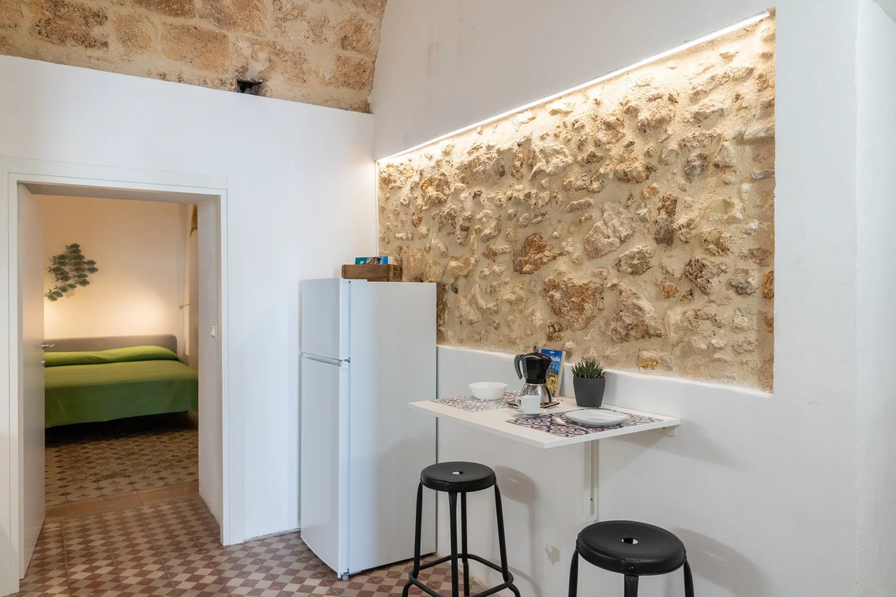 A compact dining area with a small table and stools beside a stone wall.