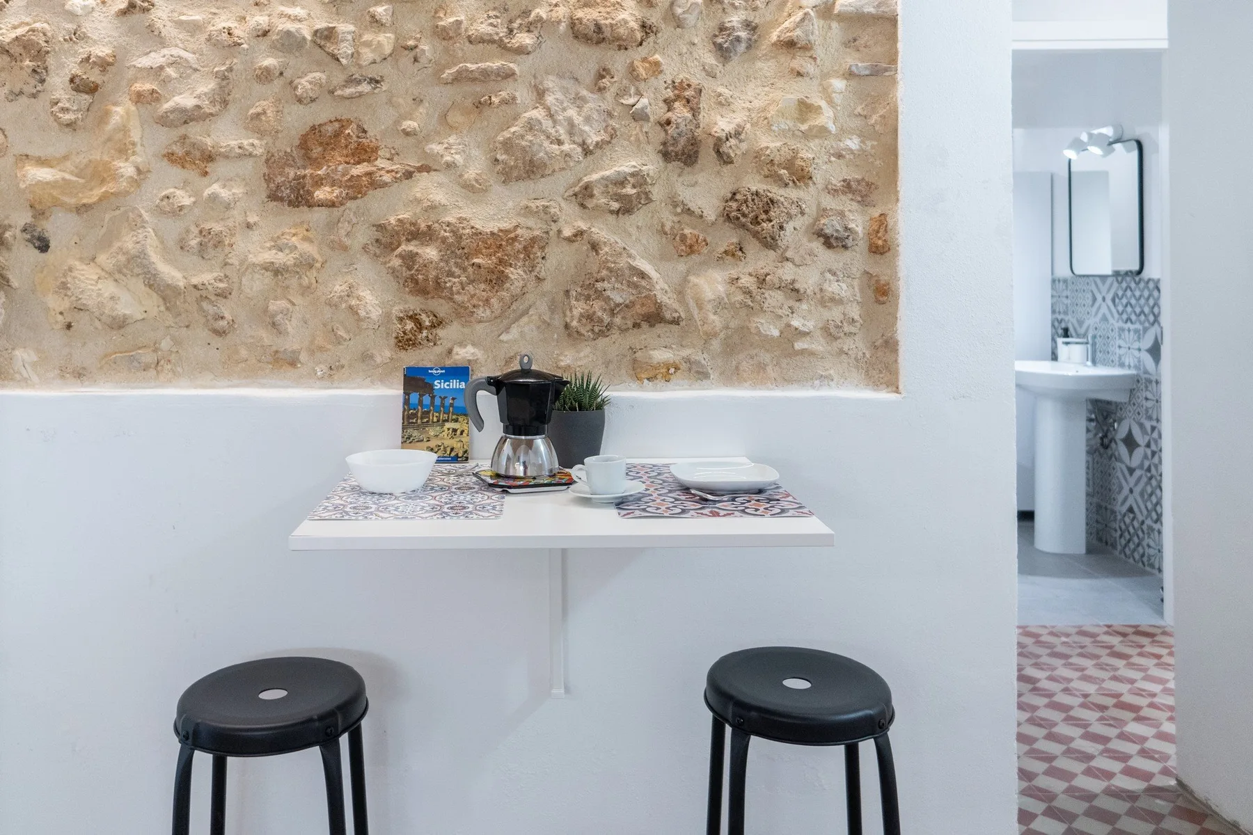 A small dining area with a wall-mounted table, dishes, and stools.