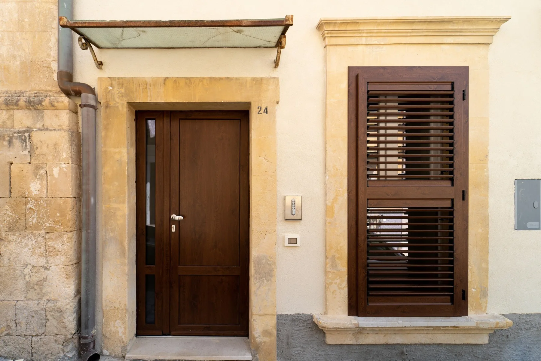 A building entrance with a dark wooden door beside a shuttered window.