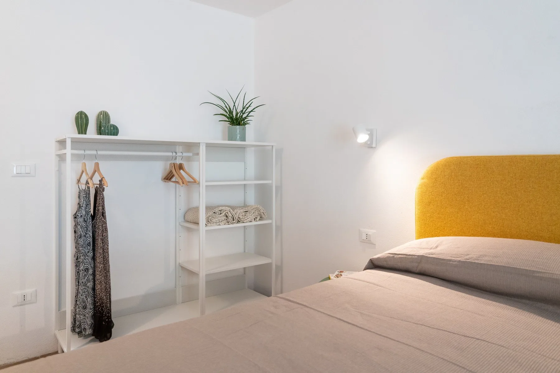 A bedroom with a bed and open clothing shelves against a white wall.