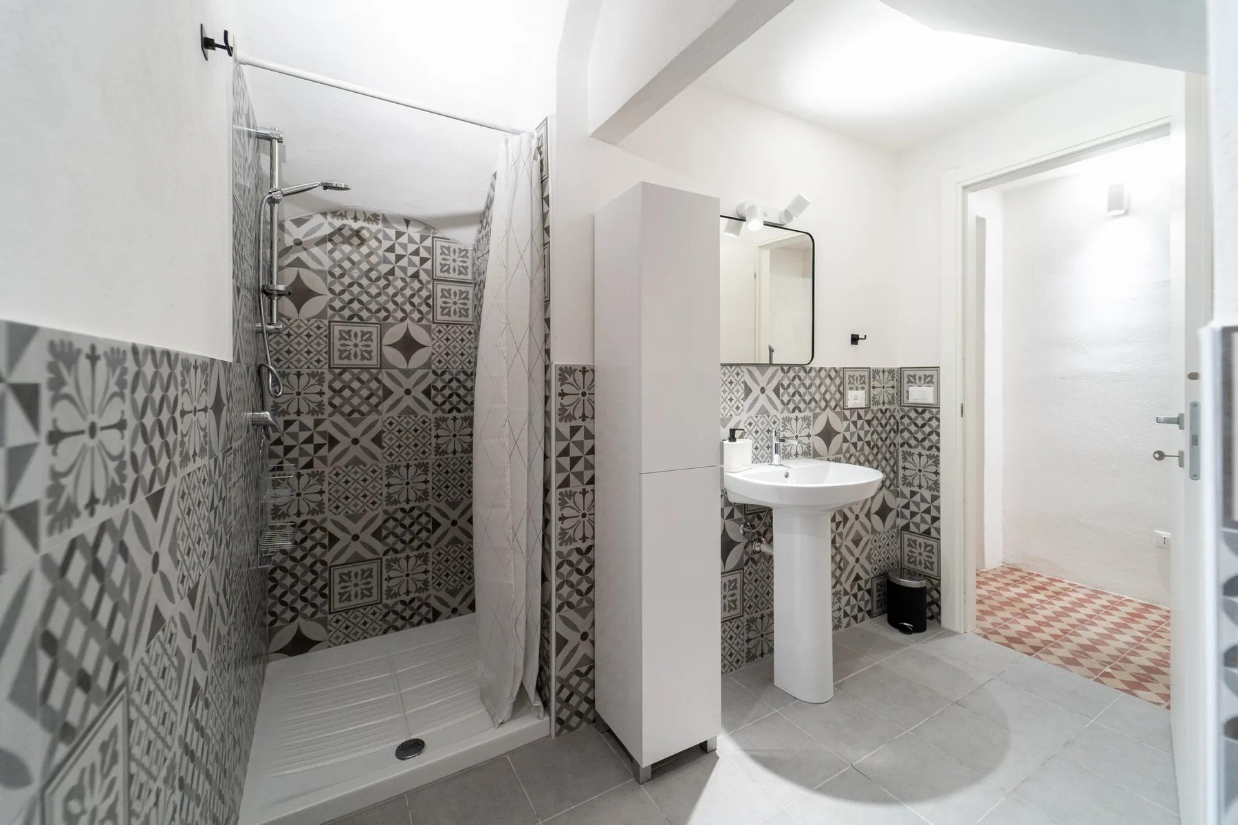 A bright bathroom with patterned wall tiles, a shower, and a sink.