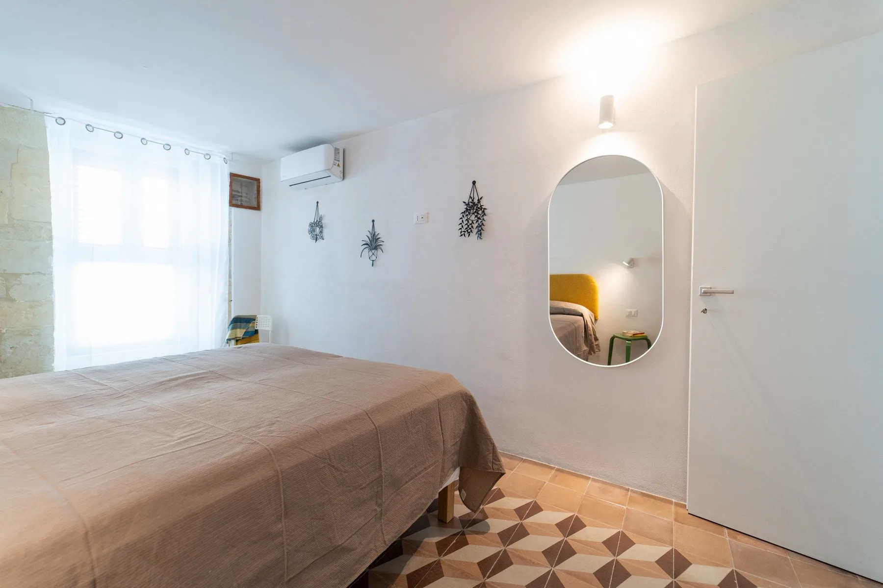 A bright bedroom with a bed beside a large window and a patterned floor.