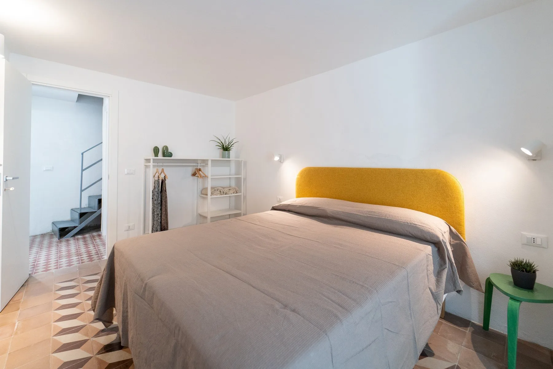A bedroom with a bed featuring a mustard-colored headboard and white walls.