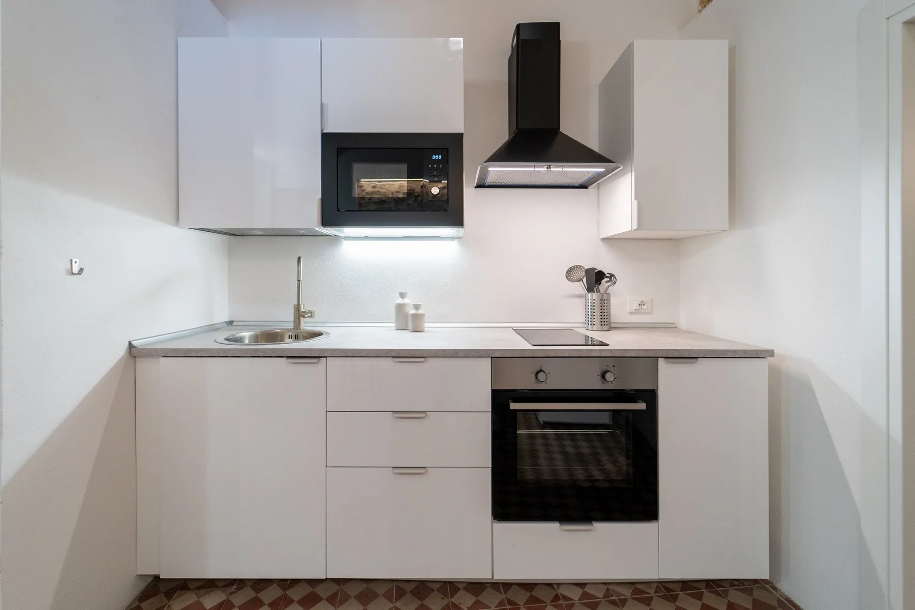 Una cocina compacta con gabinetes blancos, fregadero y horno.