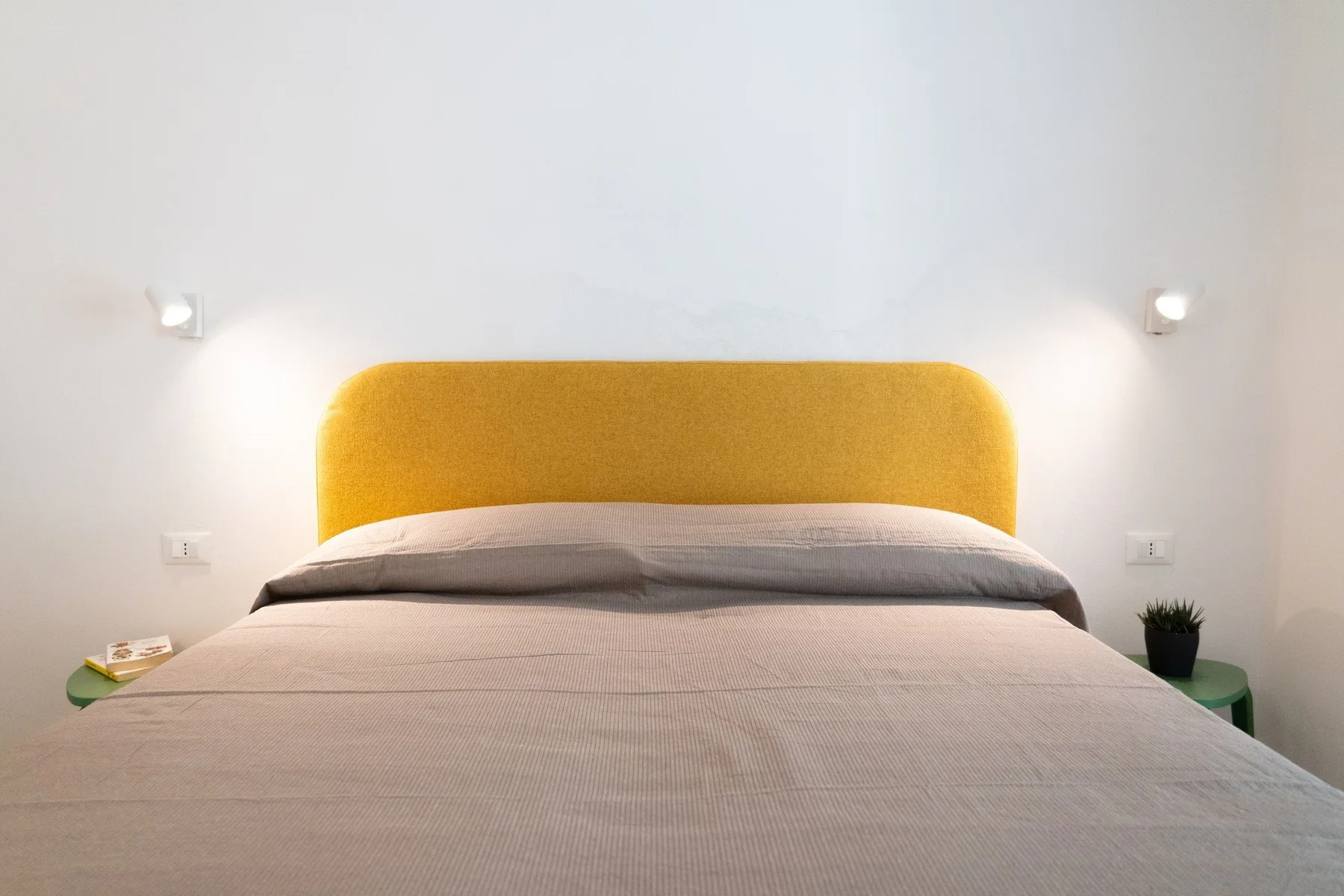 A bedroom with a bed, yellow headboard, and wall lights.