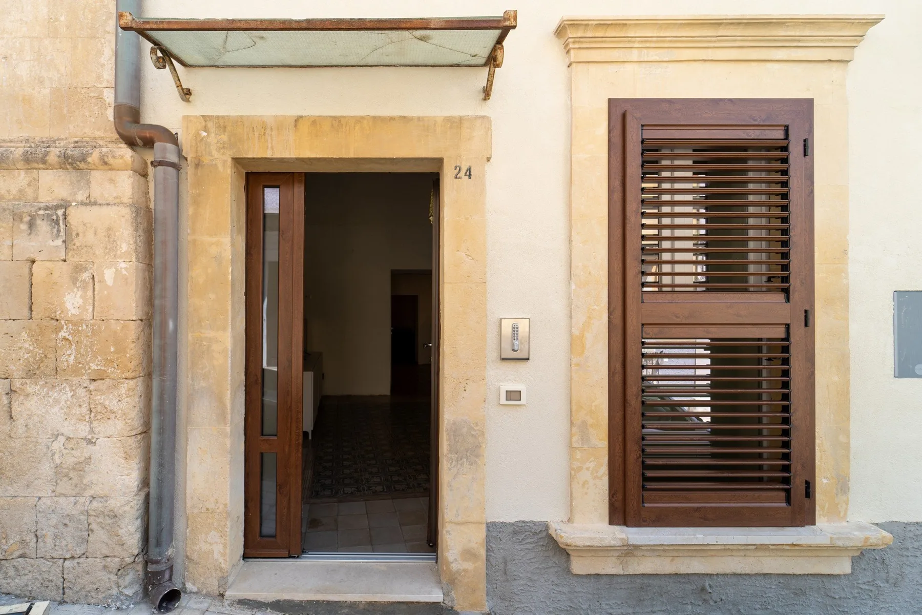 An exterior doorway and a shuttered window in a pale stone facade.