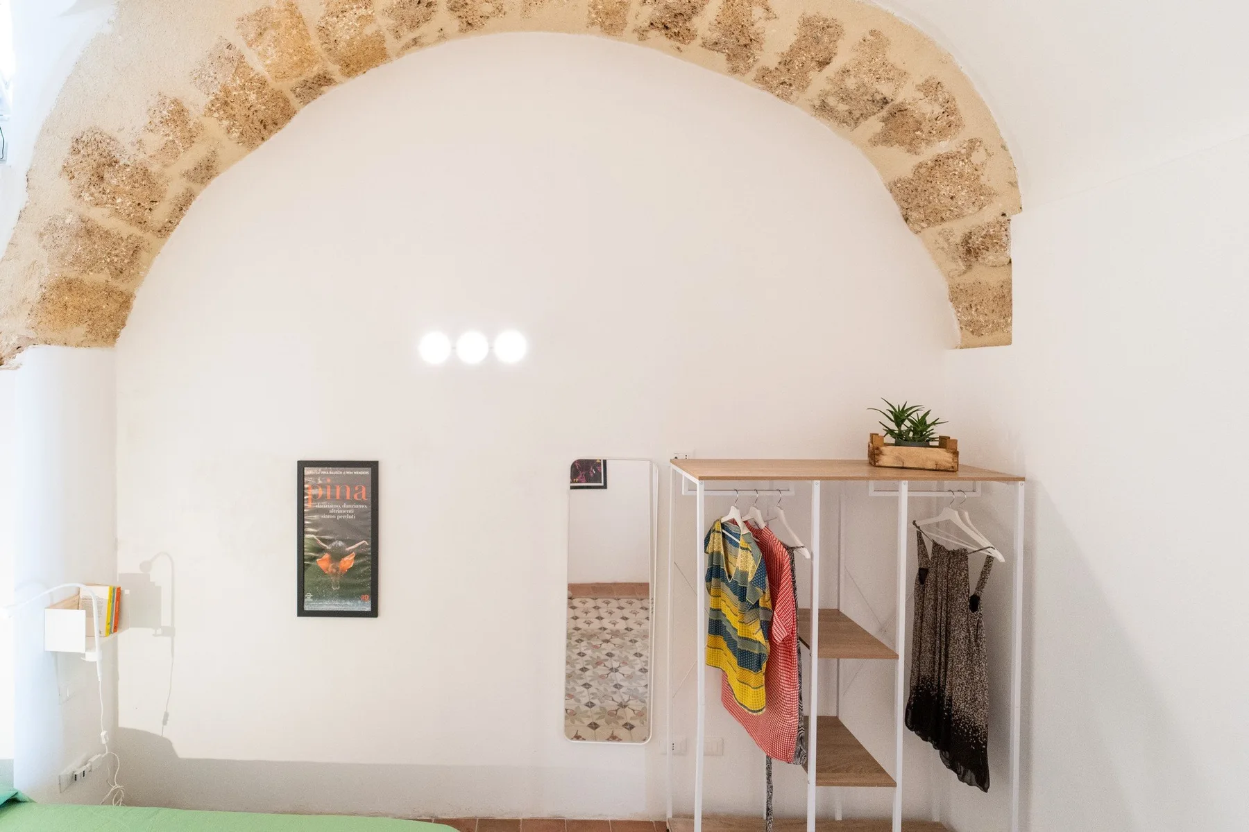 A bedroom with an open clothing rack and an arched stone detail above.