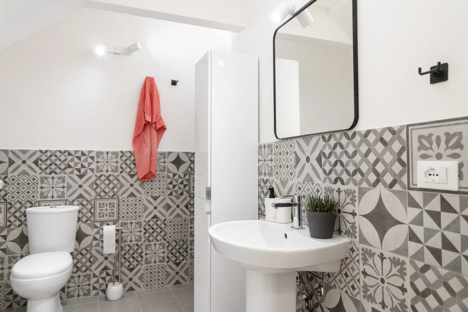 A bright bathroom with a pedestal sink, mirror, and patterned wall tiles.