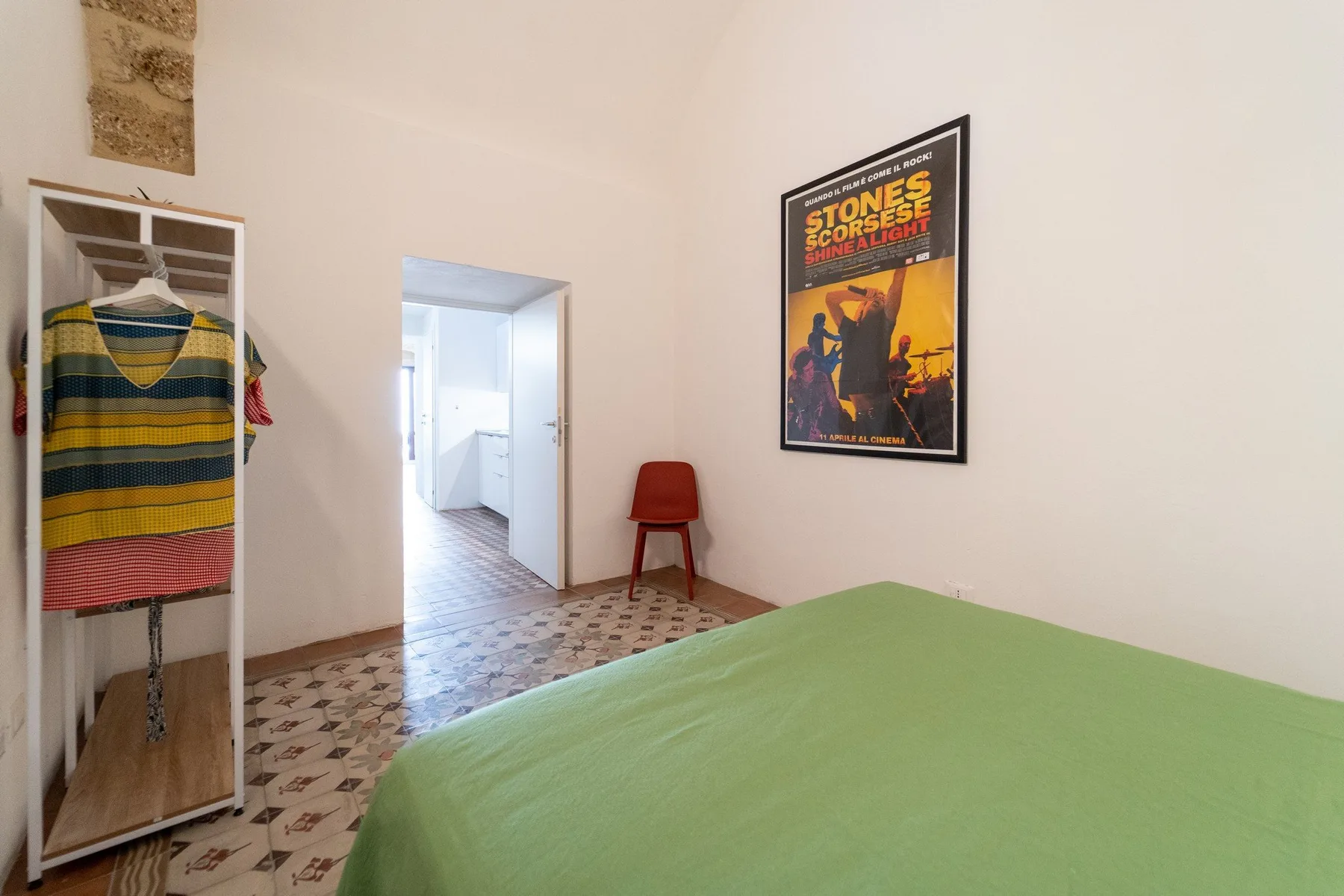 A bedroom with a green-covered bed and a doorway leading to a bright adjoining space.