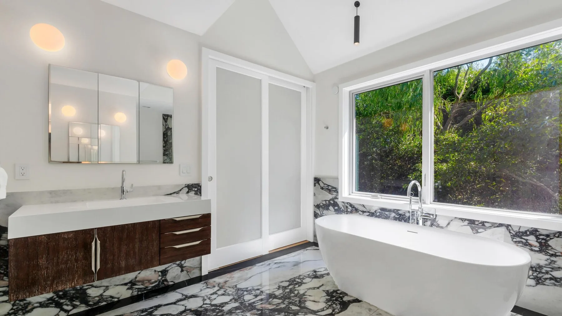 Un baño luminoso con una bañera exenta junto a una ventana grande.