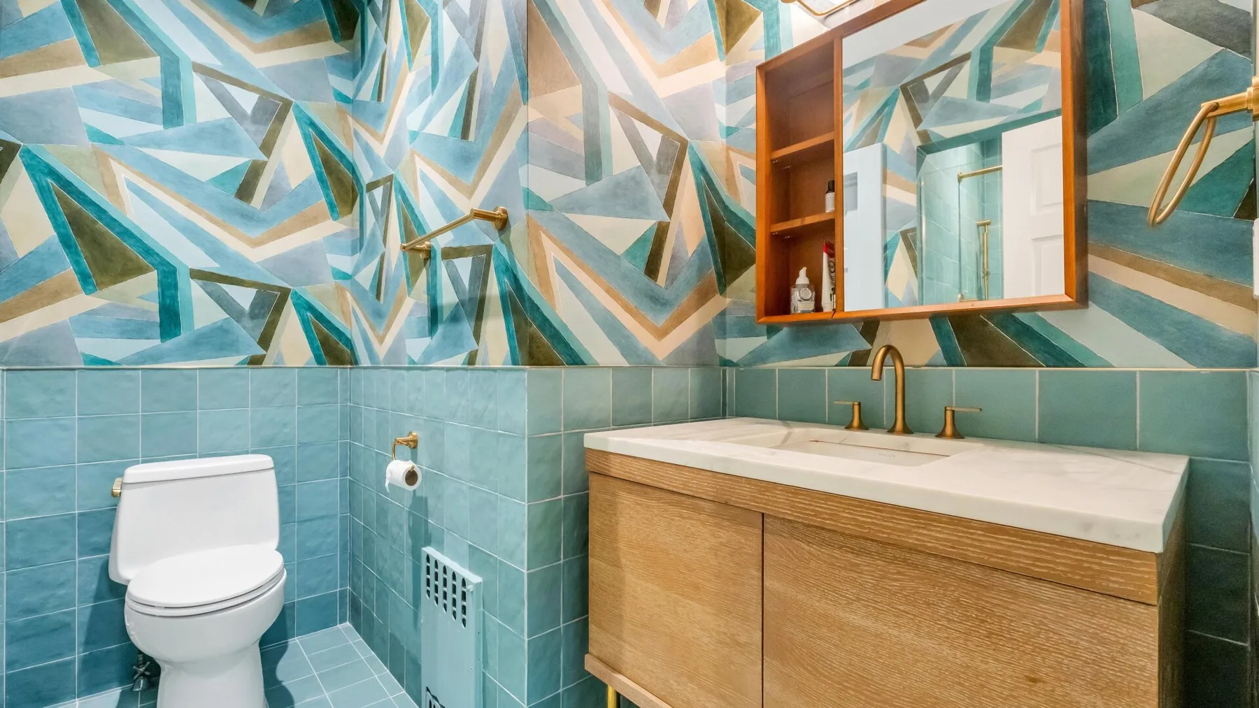 Un baño con inodoro y tocador de frente de madera bajo una pared geométrica colorida.