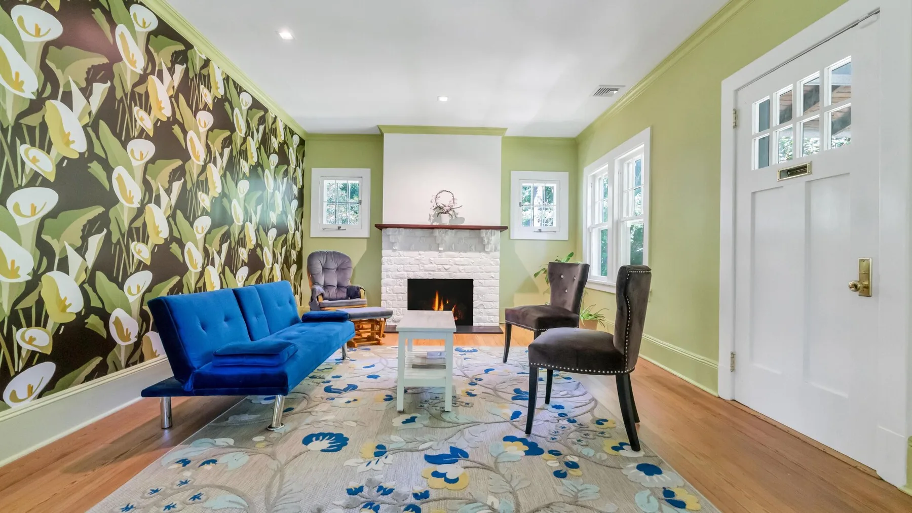 Una sala de estar con asientos azules, una chimenea y arte floral en la pared.