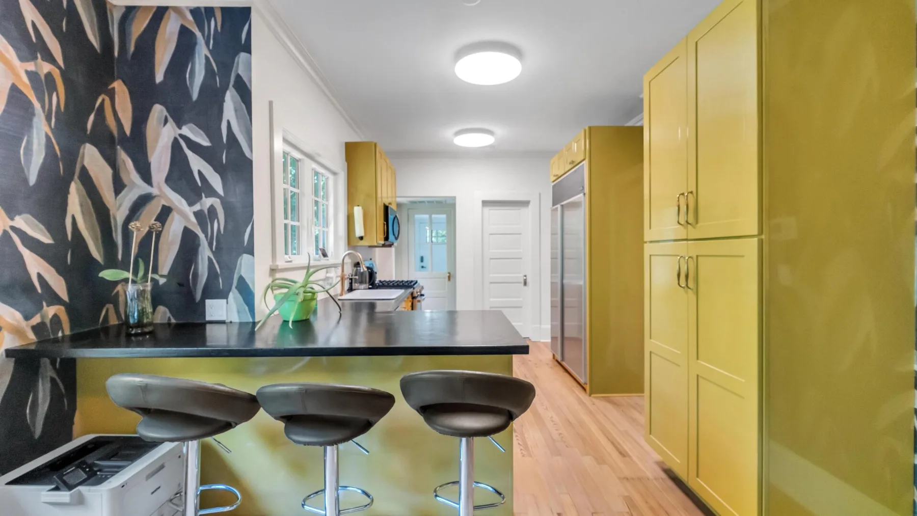 Una cocina luminosa con gabinetes amarillos, una barra larga y tres taburetes.