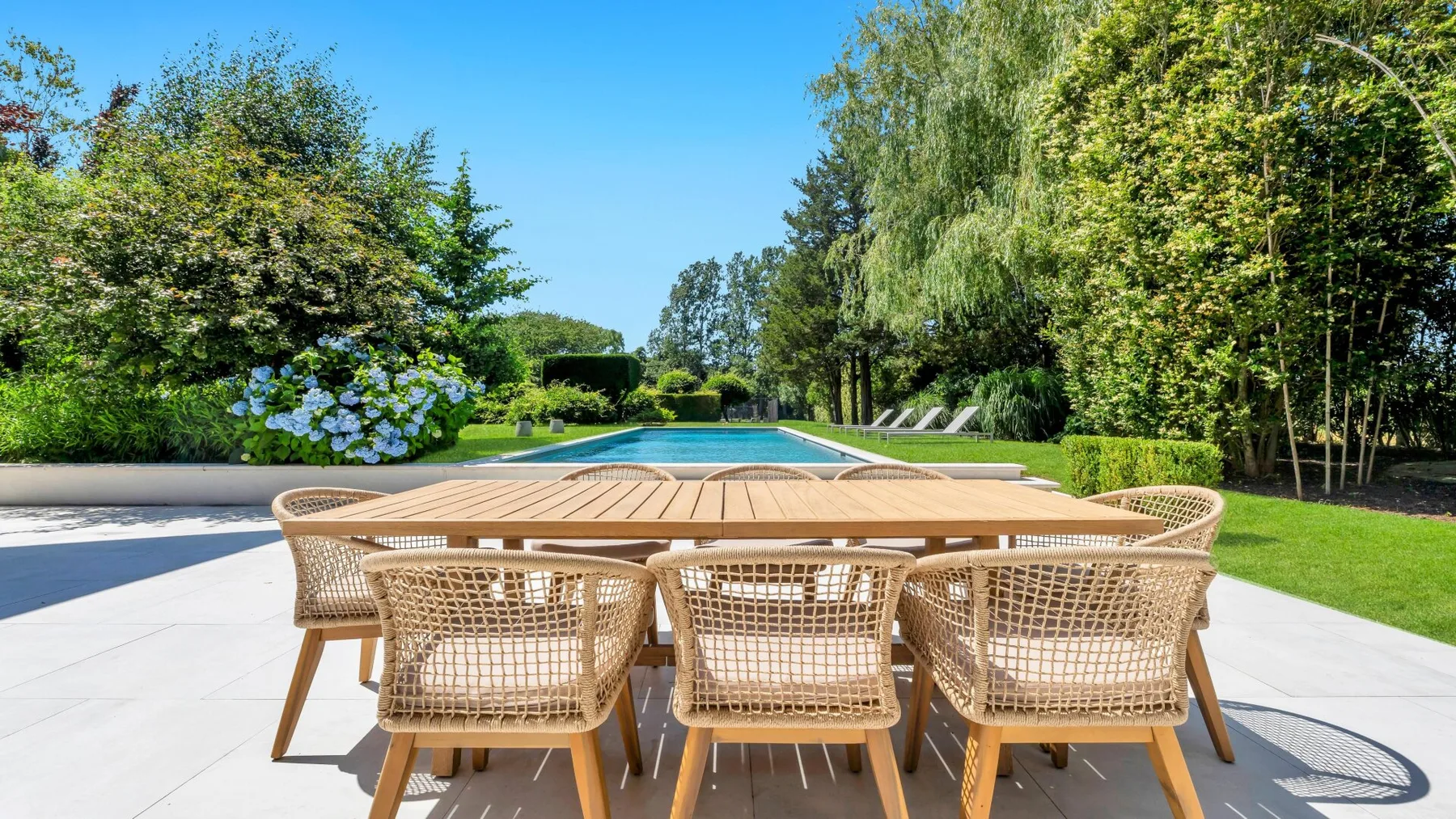 Una mesa de comedor con asientos da a una piscina rodeada de vegetación.