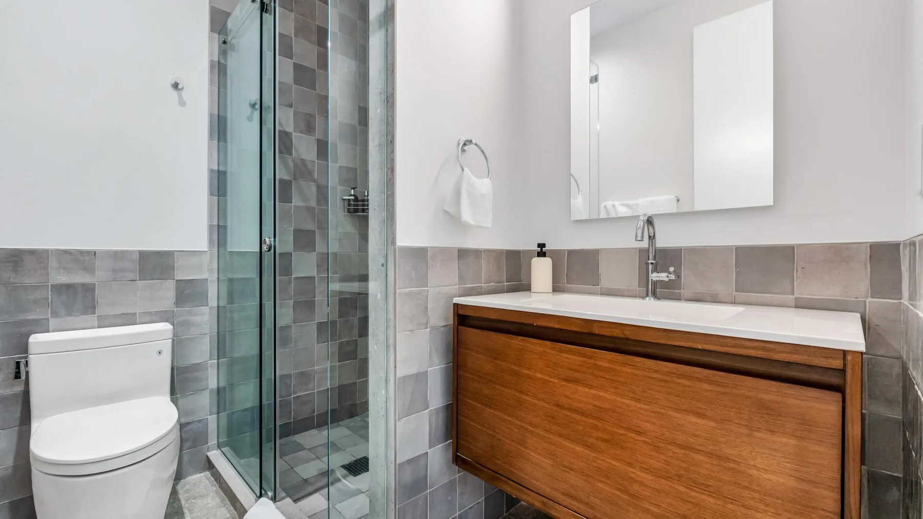 Un baño con una ducha de vidrio y un mueble de madera bajo un espejo.