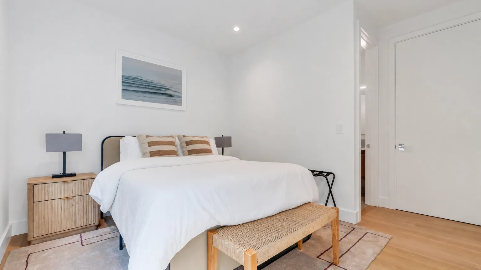 Un dormitorio luminoso con una cama tendida y una obra enmarcada en la pared.