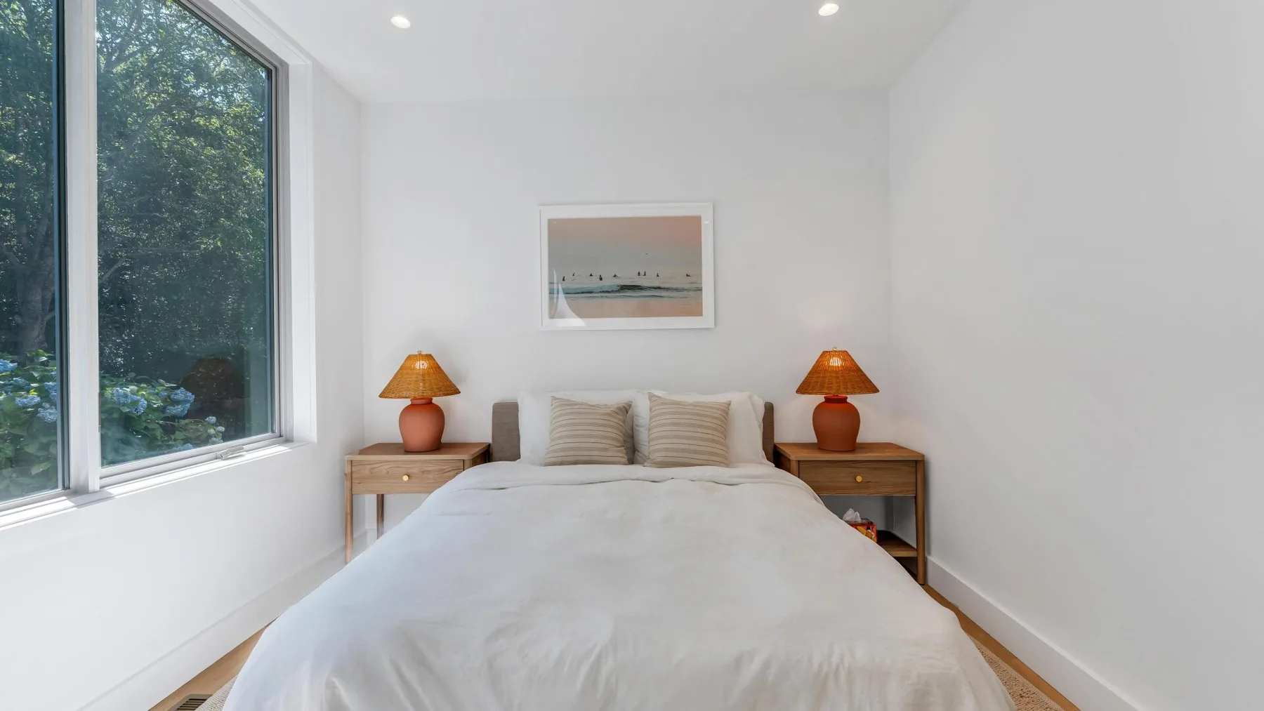 Un dormitorio luminoso con una cama entre dos mesas de noche y una ventana grande.