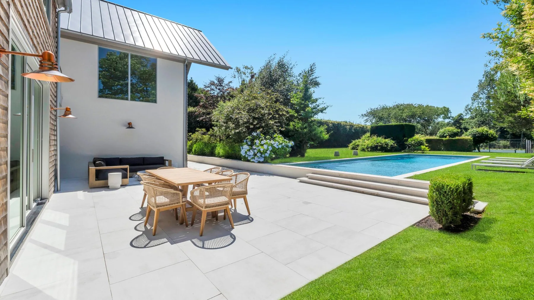 Un patio pavimentado con mesa y asientos junto a una piscina.