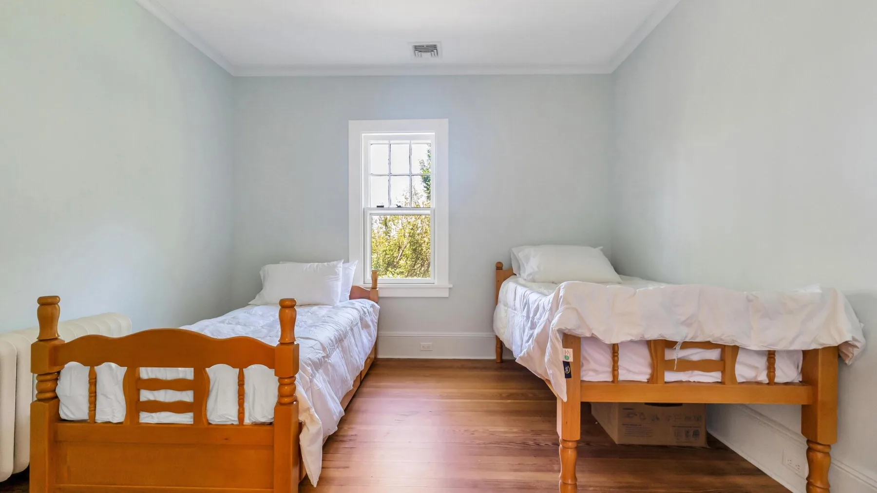 Un dormitorio con dos camas y una ventana con vegetación al fondo.