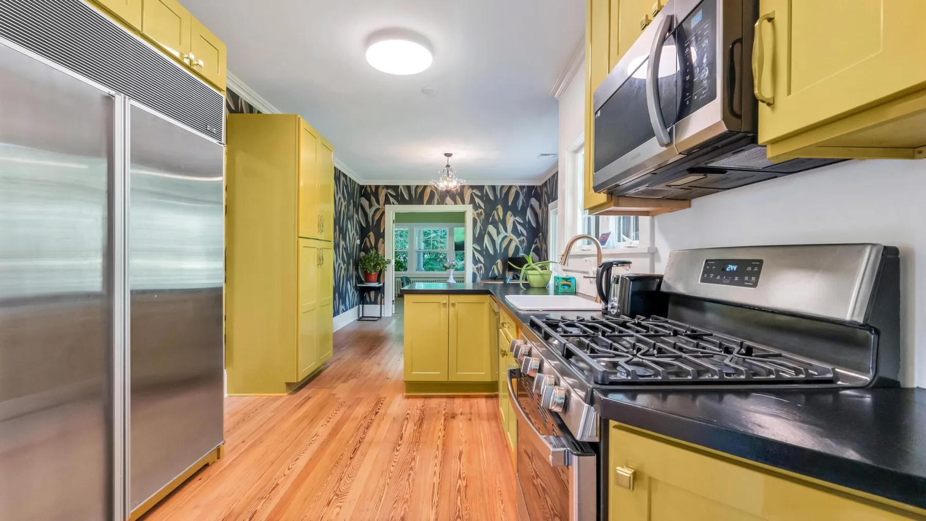 Una cocina con gabinetes amarillos, electrodomésticos de acero inoxidable y piso de tono madera.