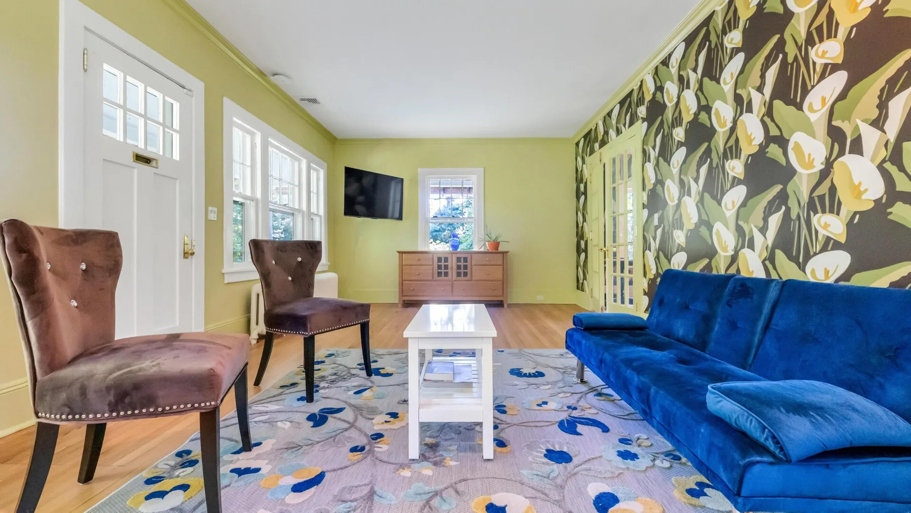 Una sala colorida con asientos azules, una mesa de centro y papel tapiz floral.