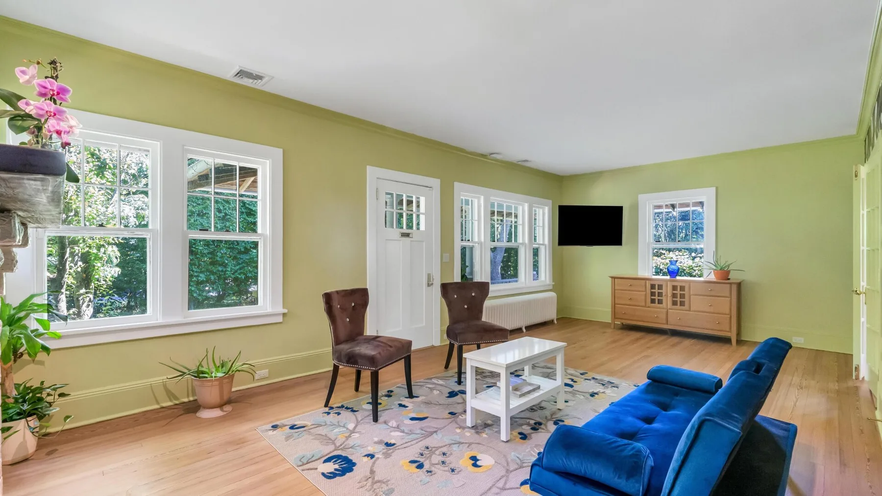 Una sala luminosa con asientos azules, una mesa de centro y ventanas grandes.