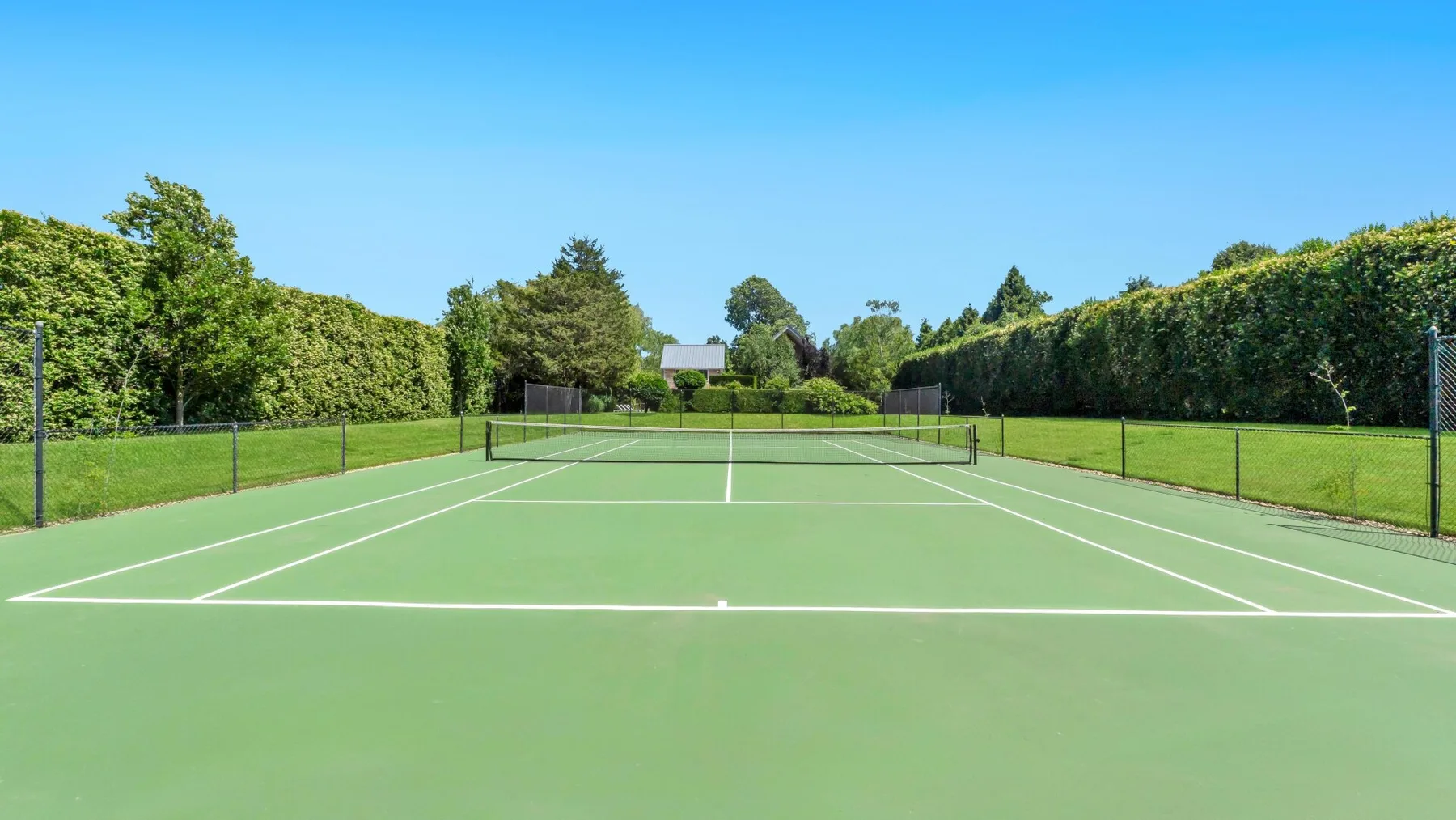 Una cancha de tenis al aire libre con una red y setos verdes alrededor.
