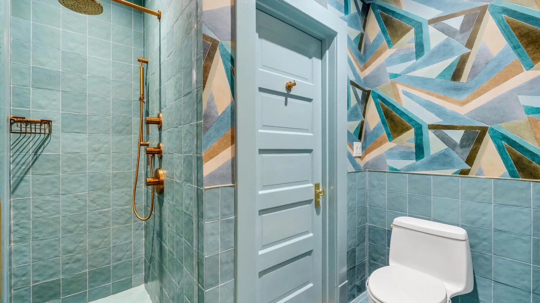 Un baño alicatado con ducha, inodoro y un colorido diseño geométrico en la pared.