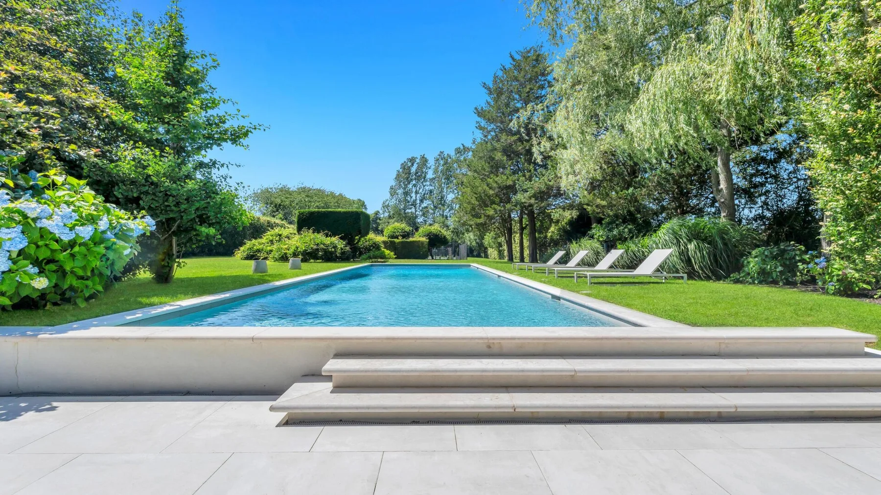 Una piscina al aire libre está rodeada de vegetación y asientos de descanso.
