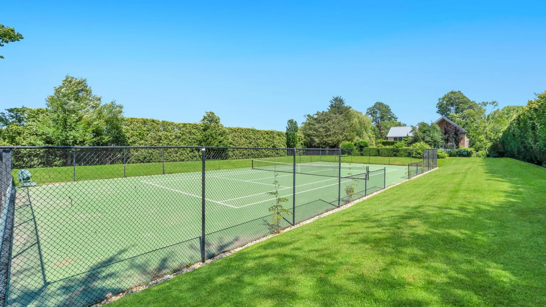 Una pista de tenis al aire libre está rodeada por una valla junto a un césped.