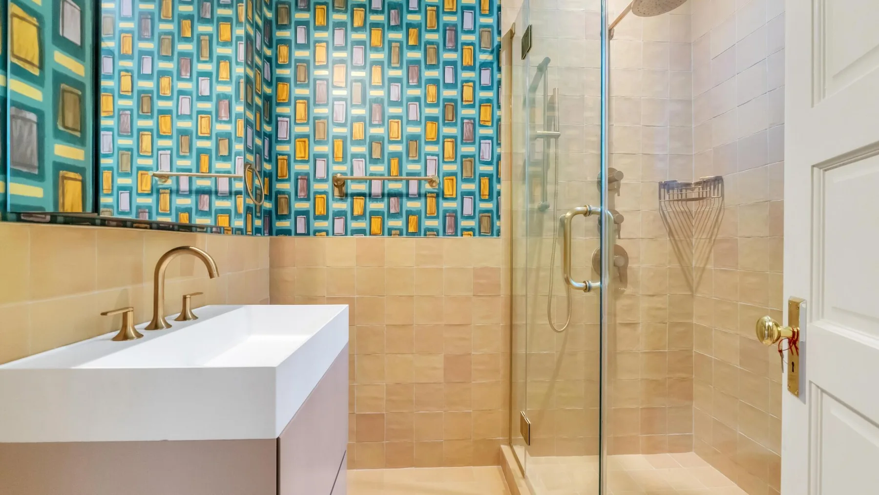 Un baño con lavabo blanco, azulejos azules estampados y una ducha de vidrio.