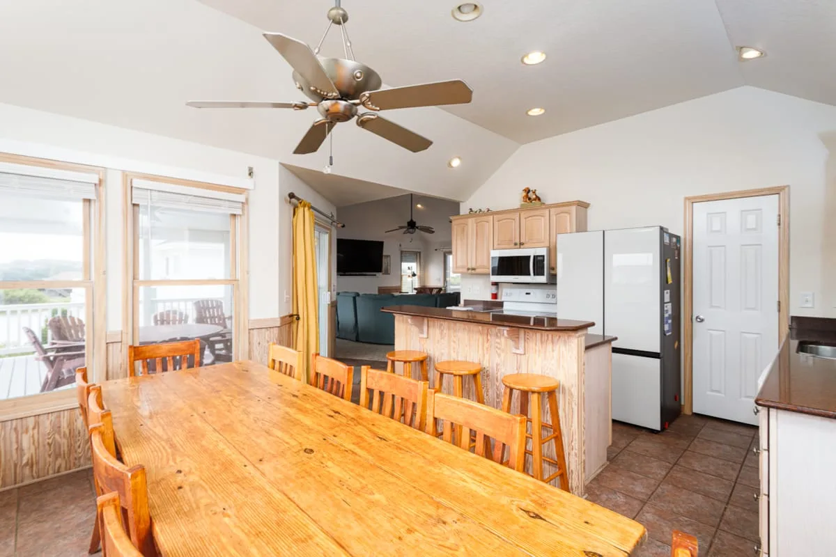 Un comedor se abre a una cocina, con una mesa de madera y taburetes.
