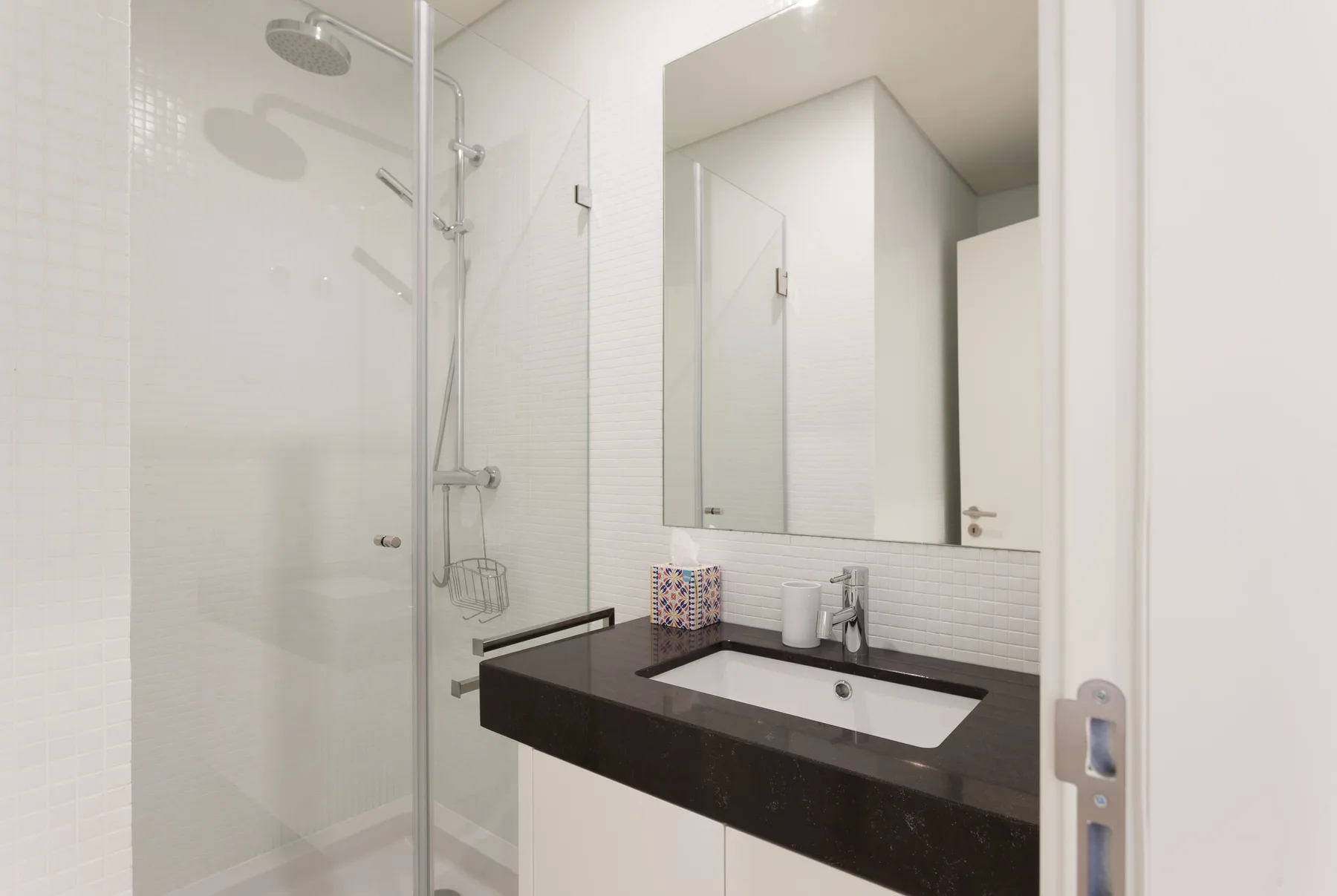 Un baño luminoso con una ducha de vidrio y una encimera oscura.