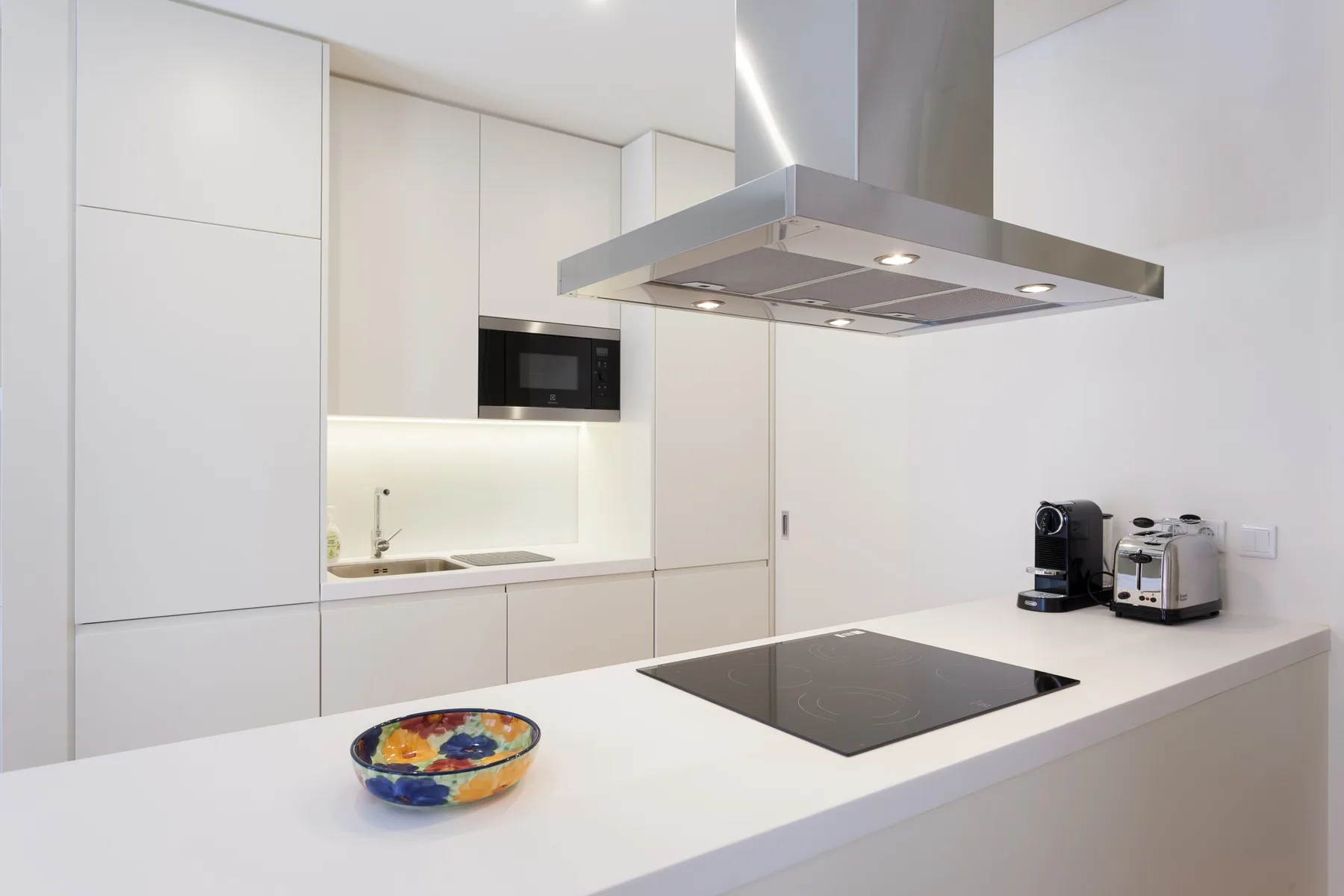 Una cocina moderna con gabinetes blancos, una placa de cocción y una campana extractora.