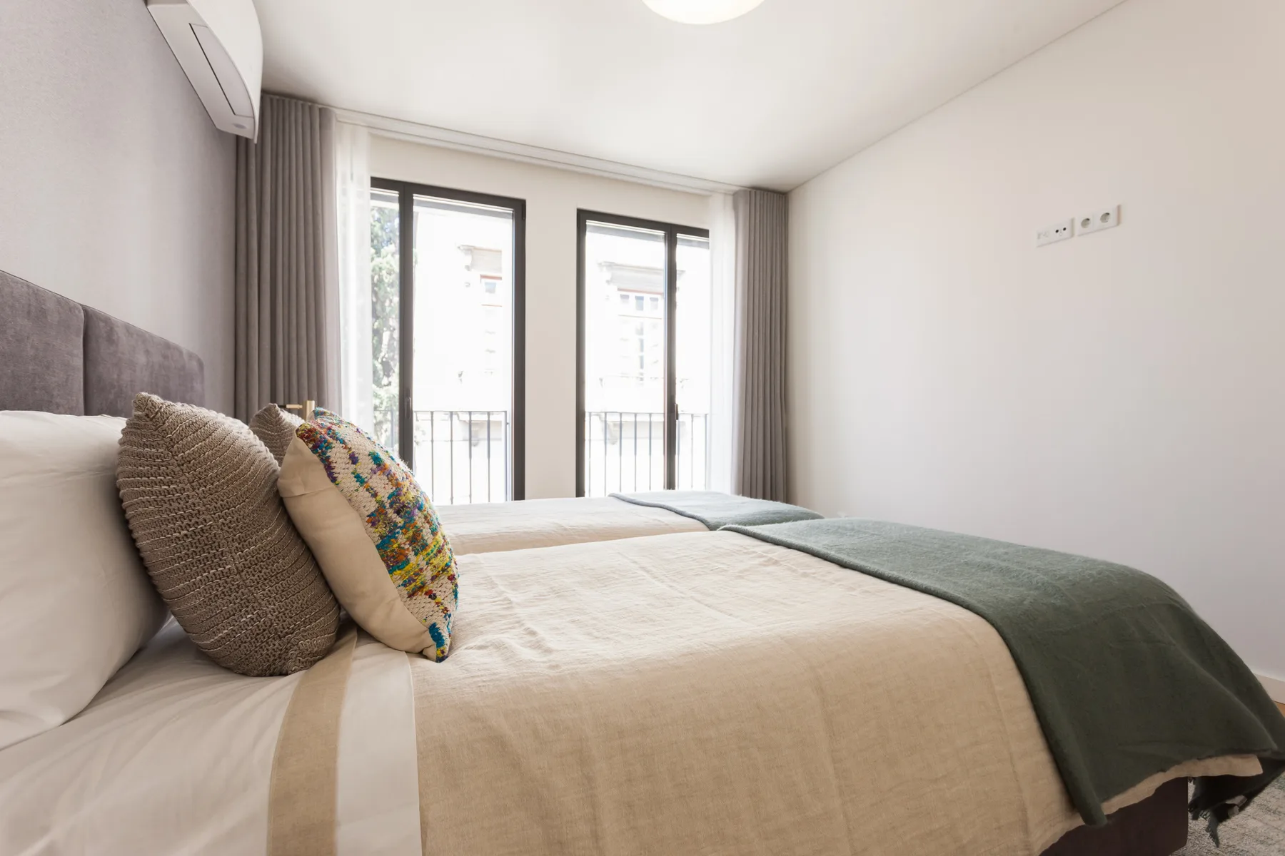 Un dormitorio con una cama, cojines estampados y ventanas altas.
