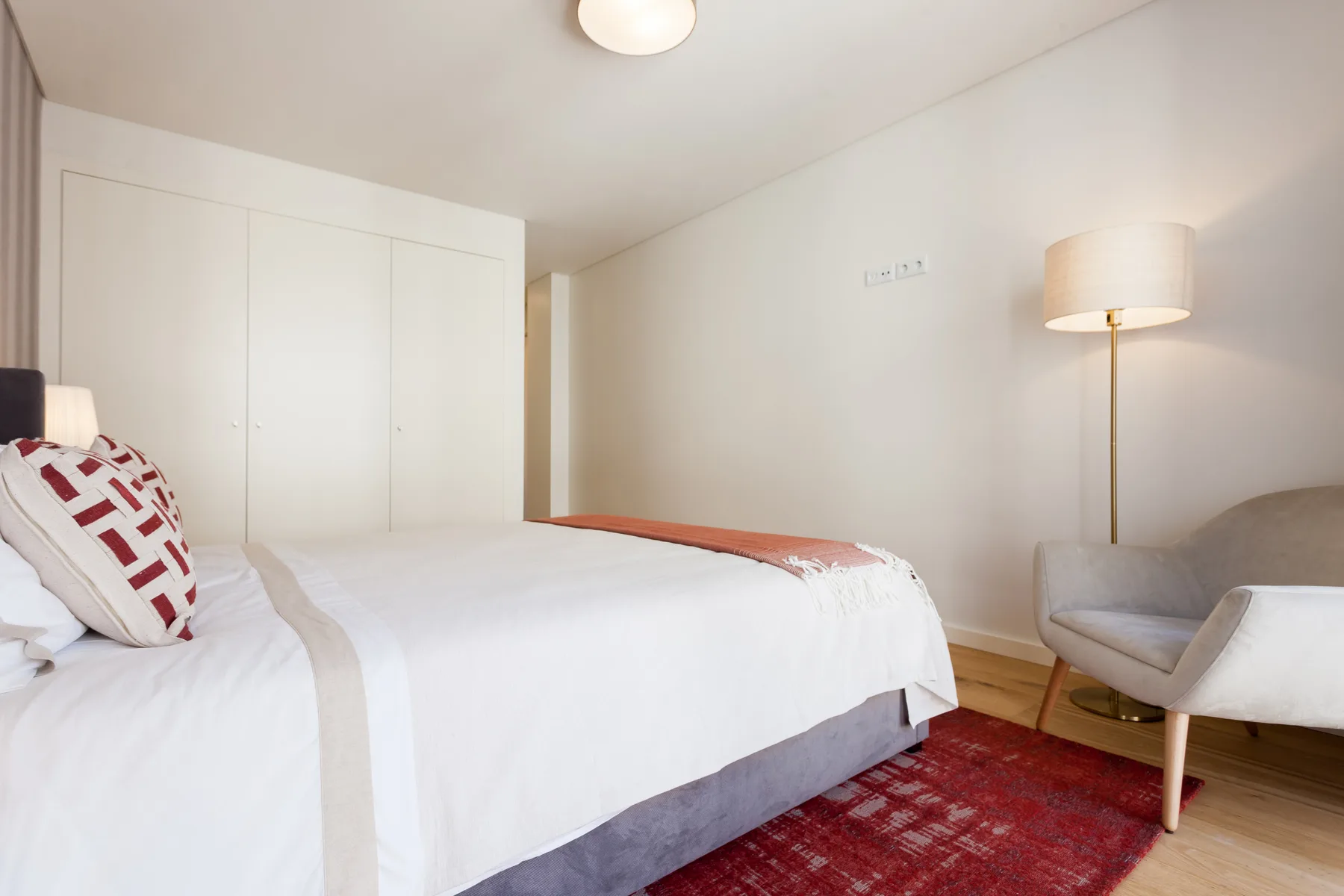 Dormitorio con una cama bien arreglada, un sillón y una lámpara de pie.