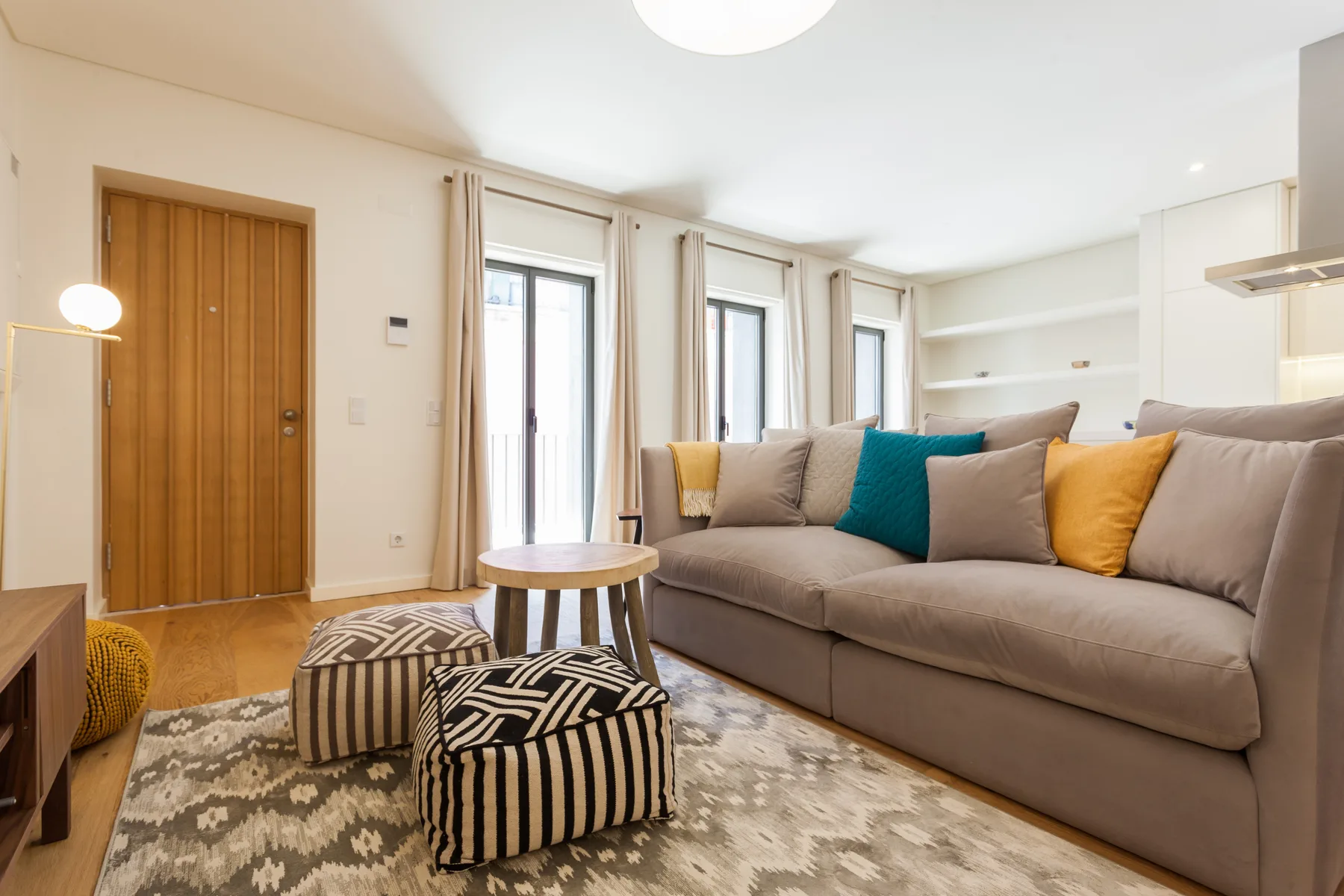 Una sala luminosa con sofá seccional, cojines de colores y una alfombra estampada.