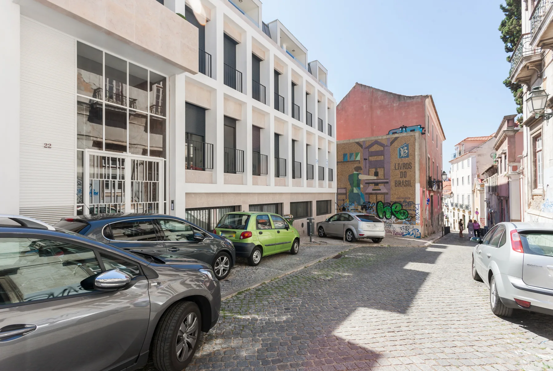 Una calle empedrada con edificios modernos, coches estacionados y un mural.